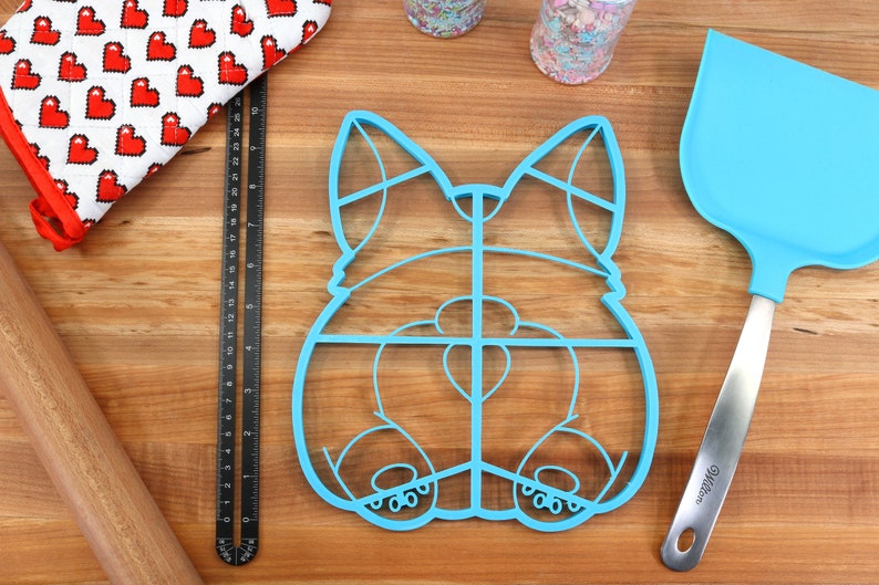 May include: Blue plastic cookie cutter shaped like a dog's rear end. The cutter has a grid pattern and is designed to make multiple cookies at once.