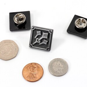 May include: Three metal pins with black backing. The center pin features a silver design of three stylized axes. The other two pins are plain black.