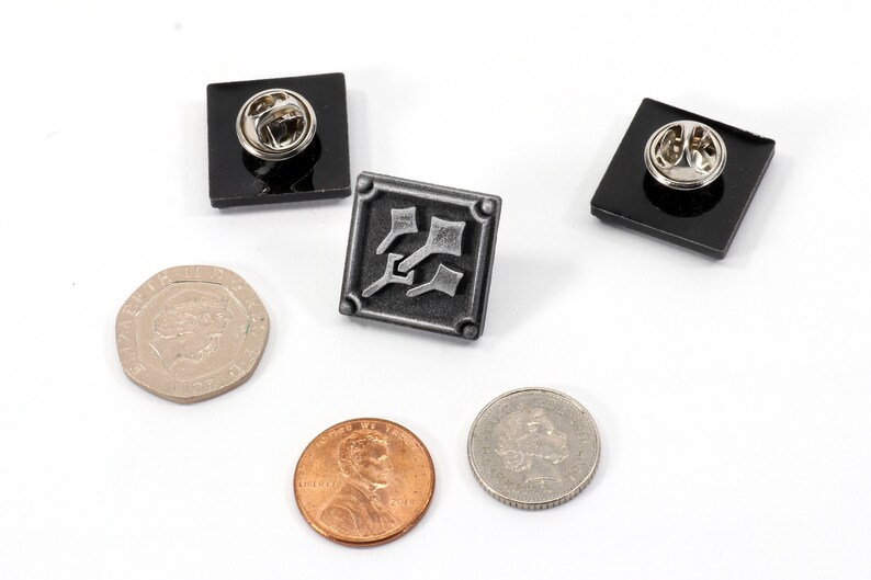 May include: Three metal pins with black backing. The center pin features a silver design of three stylized axes. The other two pins are plain black.