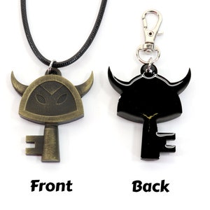 May include: A gold-colored key pendant with a horned helmet design. The key has a black silhouette on the back. The pendant is on a black cord and a silver key chain.