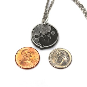 May include: A silver necklace with a yin yang pendant. The pendant is made of metal and has a black and white design. The necklace is shown with two US coins for size comparison.