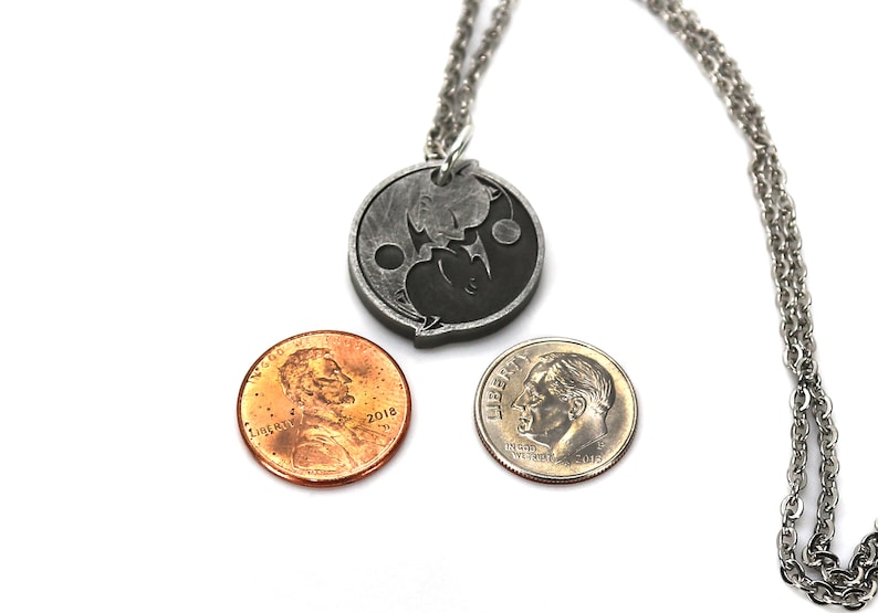 May include: A silver necklace with a yin yang pendant. The pendant is made of metal and has a black and white design. The necklace is shown with two US coins for size comparison.