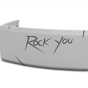 May include: A light gray, curved object with the words "Rock You" etched into the front. The object has a rectangular shape with rounded corners and appears to be made of a solid material. There are several lines etched into the surface.