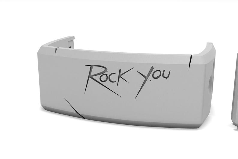 May include: A light gray, curved object with the words "Rock You" etched into the front. The object has a rectangular shape with rounded corners and appears to be made of a solid material. There are several lines etched into the surface.