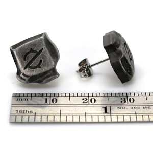 May include: A pair of silver stud earrings with a textured, square-shaped design. Each earring features a stylized letter "Z" in the center.