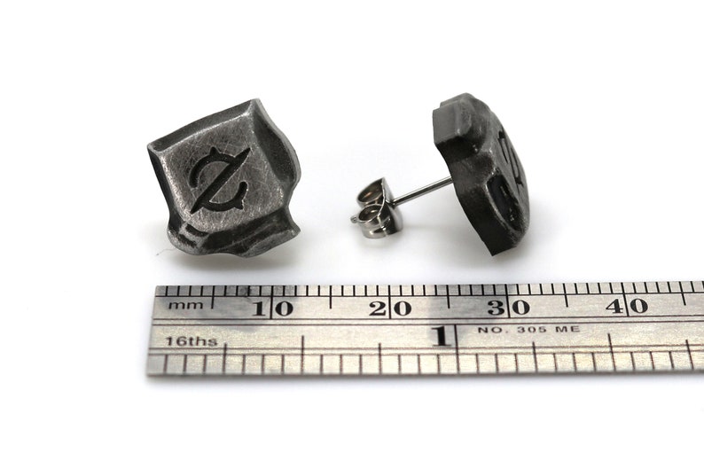 May include: A pair of silver stud earrings with a textured, square-shaped design. Each earring features a stylized letter "Z" in the center.