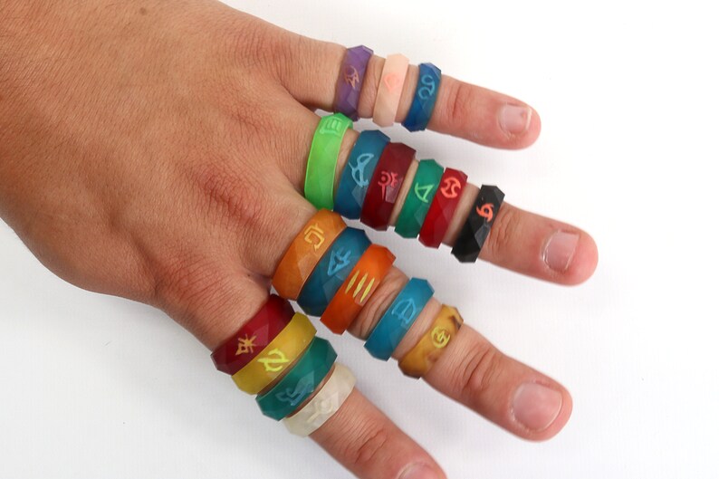 May include: A hand wearing a variety of colorful silicone rings with different symbols and designs. The rings are stacked on each finger.