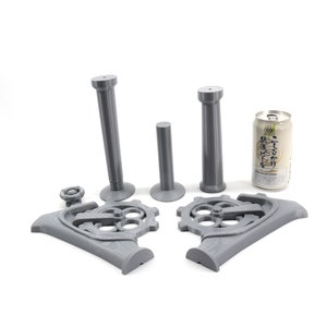May include: A 3D printed gray metal steampunk-style can holder with two tall pillars and a base with gears. The holder is designed to hold a standard-sized can.