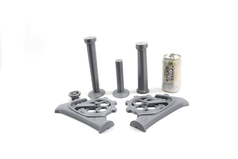 May include: A 3D printed gray metal steampunk-style can holder with two tall pillars and a base with gears. The holder is designed to hold a standard-sized can.