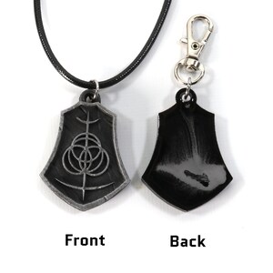 May include: A black leather necklace with a silver pendant featuring a geometric design. The pendant is shaped like a shield and has a black back.