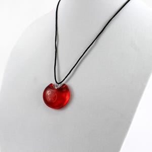 May include: A red heart-shaped pendant necklace with a black cord. The pendant has a silver bail and a small design inside.