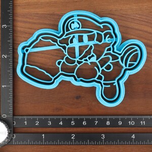 May include: Blue plastic cookie cutter shaped like a cartoon character wearing a hat. The character is holding a large object in its left hand.