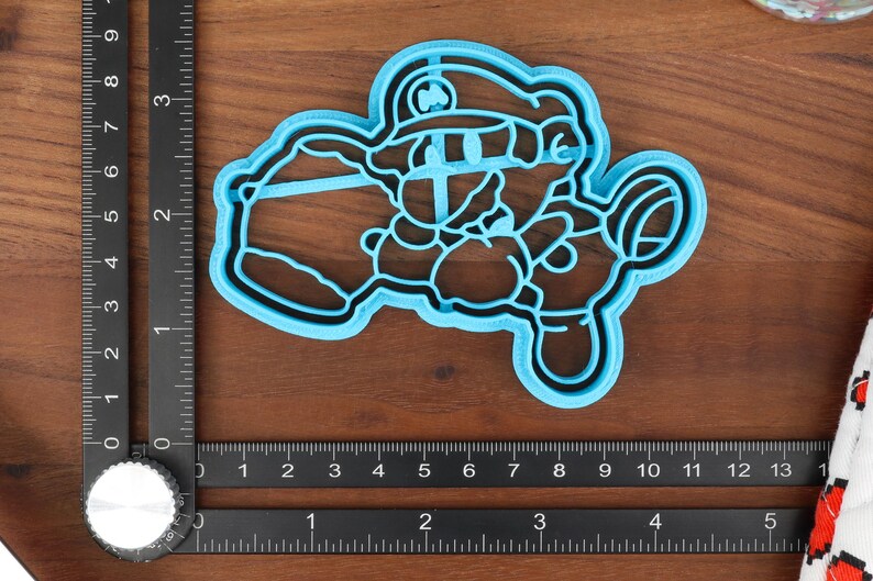 May include: Blue plastic cookie cutter shaped like a cartoon character wearing a hat. The character is holding a large object in its left hand.
