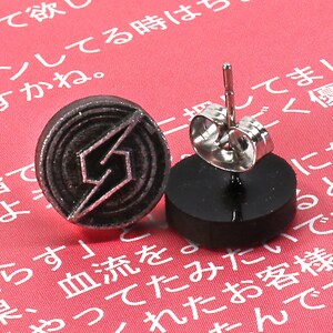 May include: A pair of silver stud earrings with a black circular design featuring a stylised lightning bolt. The earrings are displayed on a red surface.