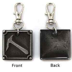 May include: A metal keychain with a silver clasp. The front of the square pendant features a pickaxe design, while the back is a solid, textured gray. The word "Front" is below the pickaxe, and "Back" is on the other side.