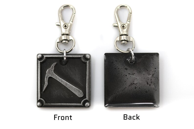 May include: A metal keychain with a silver clasp. The front of the square pendant features a pickaxe design, while the back is a solid, textured gray. The word "Front" is below the pickaxe, and "Back" is on the other side.