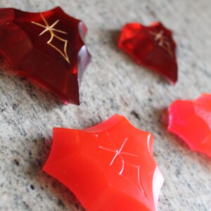 May include: Four red, star-shaped, translucent, decorative pieces with a gold design.