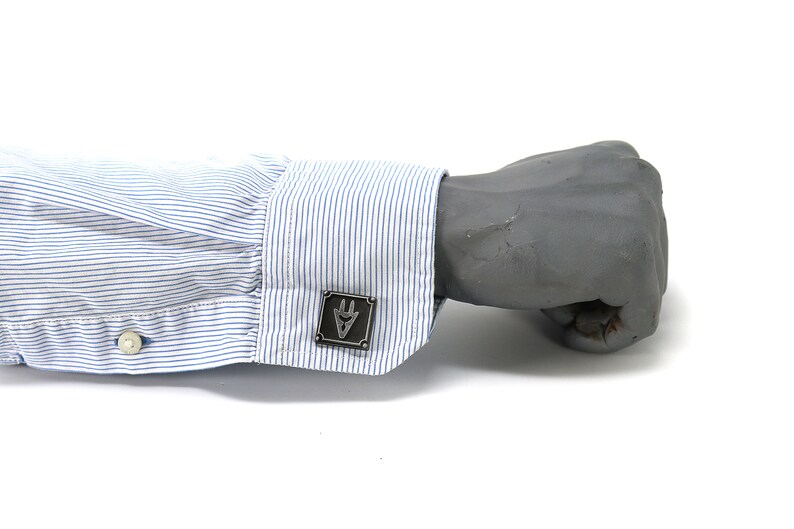 May include: A pair of cufflinks with a silver finish and a geometric design. The cufflinks are on a blue and white striped shirt cuff.