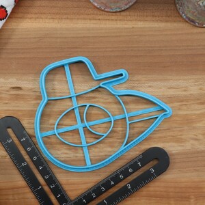 May include: A blue plastic cookie cutter shaped like a Star Wars X-Wing fighter. The cutter has a detailed design with a cross-shaped interior.