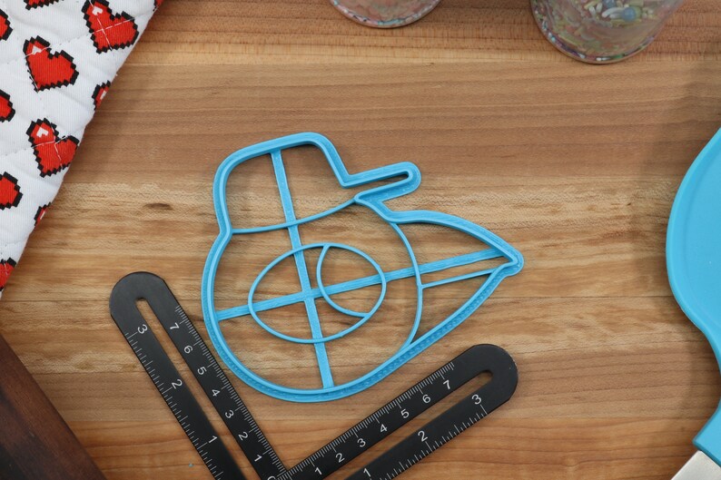 May include: A blue plastic cookie cutter shaped like a Star Wars X-Wing fighter. The cutter has a detailed design with a cross-shaped interior.