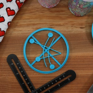 May include: A blue plastic circle cookie cutter with a design of four circles connected by lines. The cookie cutter is on a wooden surface.