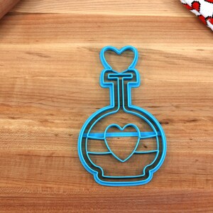 May include: Blue plastic cookie cutter shaped like a bottle with a heart on the top and a heart inside the bottle.