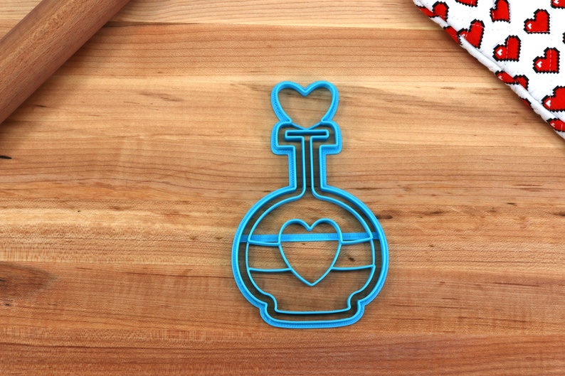 May include: Blue plastic cookie cutter shaped like a bottle with a heart on the top and a heart inside the bottle.