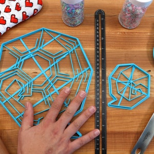 May include: Two blue plastic cookie cutters in the shape of snowflakes on a wooden surface. The larger cutter has a more intricate design than the smaller cutter.