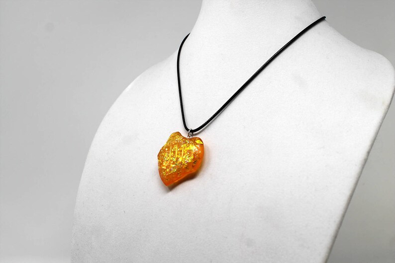 May include: A gold and orange heart-shaped pendant necklace on a black cord.