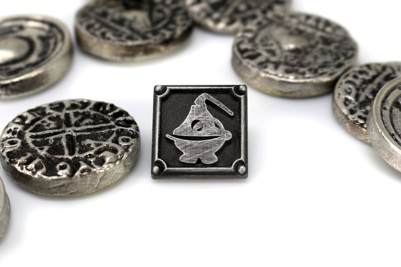 May include: A silver metal pin with a square design. The pin features a black background with a silver metal image of a stylized cauldron with a handle.