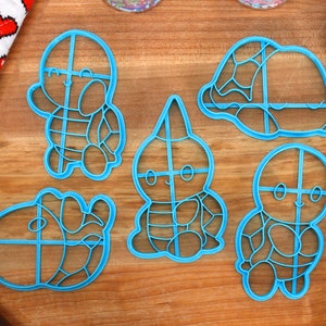 May include: Five blue plastic cookie cutters shaped like turtles with different designs. The cutters have a grid pattern on them.