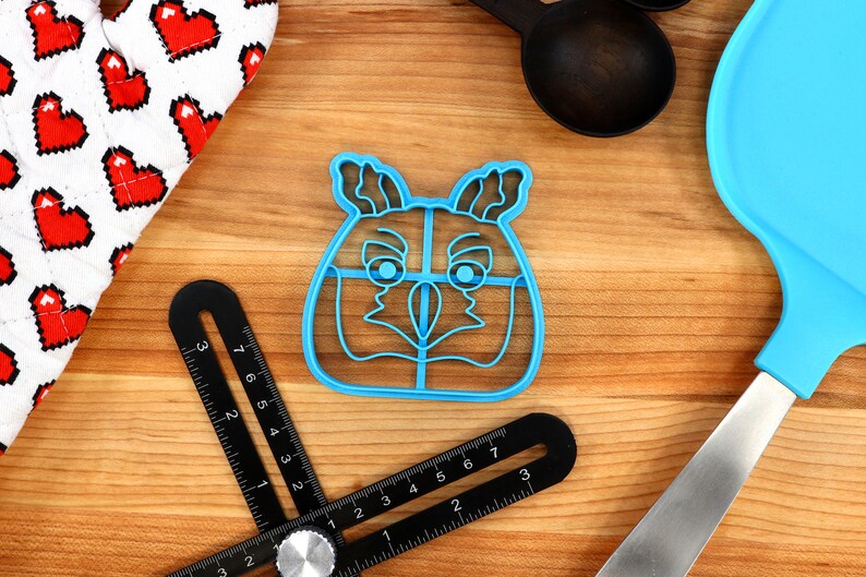 May include: A blue plastic cookie cutter shaped like an owl's face. The cutter has a detailed design with eyes, beak, and feathers.