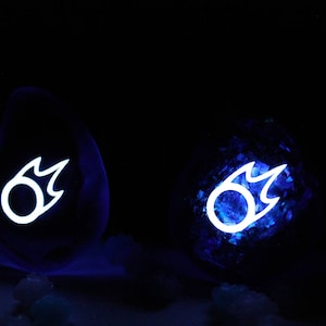 May include: Two blue glass orbs with a white glowing symbol of a flame inside. The orbs are sitting on a dark surface.