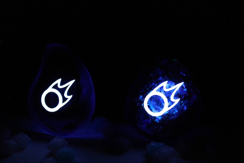 May include: Two blue glass orbs with a white glowing symbol of a flame inside. The orbs are sitting on a dark surface.