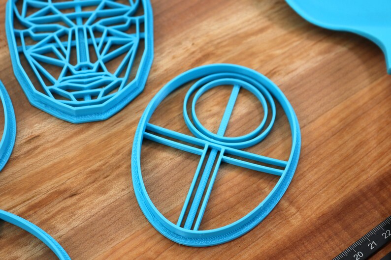May include: A set of blue plastic cookie cutters, including a face, a circle with a cross inside, and an oval with a circle and cross inside.