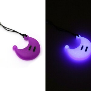 May include: A purple crescent moon-shaped keychain with a black string and a silver clip. The keychain glows in the dark, emitting a bright purple light.