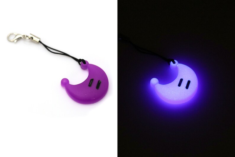 May include: A purple crescent moon-shaped keychain with a black string and a silver clip. The keychain glows in the dark, emitting a bright purple light.
