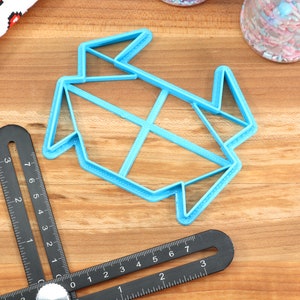May include: A blue plastic cookie cutter shaped like a folded origami crane. The cutter is on a wooden surface.