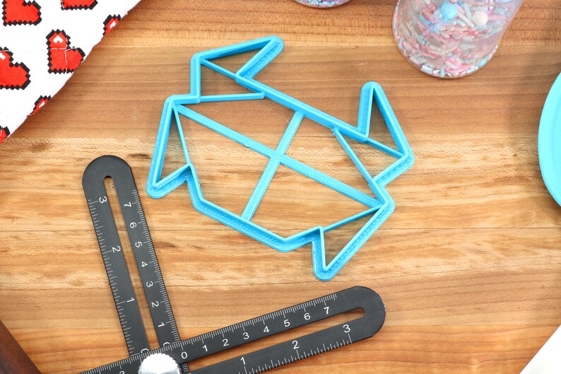 May include: A blue plastic cookie cutter shaped like a folded origami crane. The cutter is on a wooden surface.