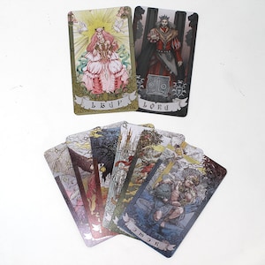 May include: A set of tarot cards featuring illustrations of people and scenes. The cards are in a variety of colors, including gold, silver, and black. The cards are arranged in a fan shape, with the top card showing a woman in a pink dress. The text on the cards includes the words "Lord" and "Cup".