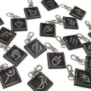May include: A set of 16 silver keychains with different symbols on each. The keychains are black with silver accents and are all square shaped.