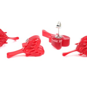 May include: A pair of red heart-shaped earrings with a flame design. The earrings are made of resin and have a silver post.