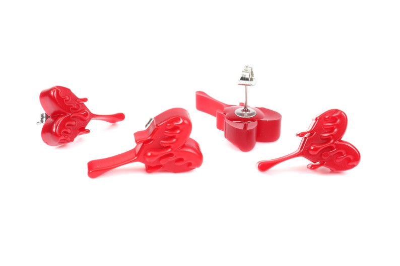 May include: A pair of red heart-shaped earrings with a flame design. The earrings are made of resin and have a silver post.