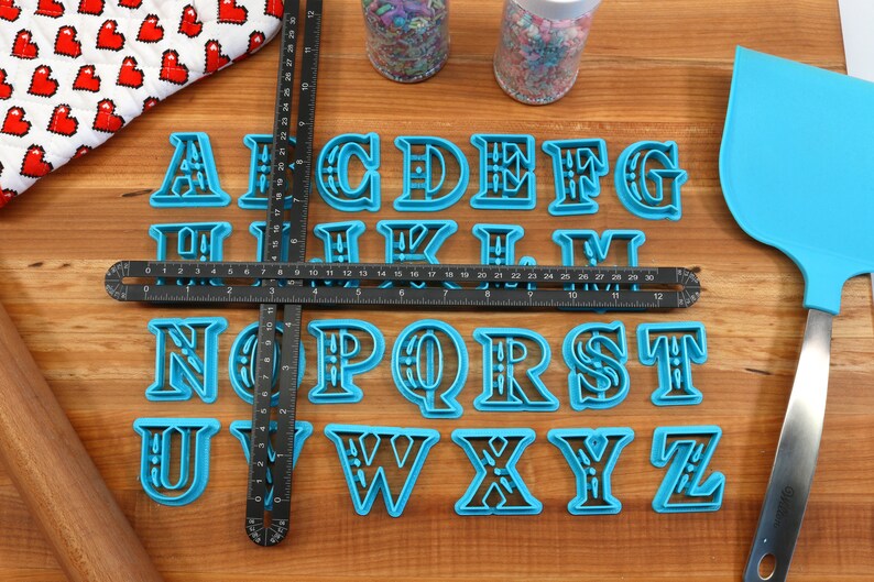May include: A set of blue plastic alphabet cookie cutters on a wooden surface. The cutters are arranged in alphabetical order.