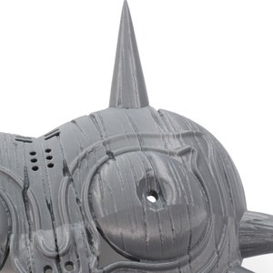 May include: A gray 3D printed mask with a sharp, pointed design. The mask has two large, round eyes and a series of small holes on the side.