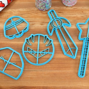 May include: A set of five blue plastic cookie cutters shaped like a knight's helmet, a knight's face, a sword, a star-shaped wand, and a shield.