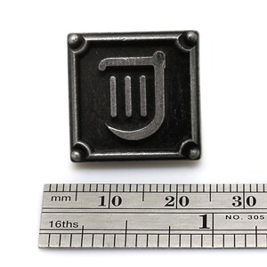 Puede incluir: Un pin de metal plateado con fondo negro y un s&iacute;mbolo de arpa plateado. El pin mide aproximadamente 2 cm de ancho.