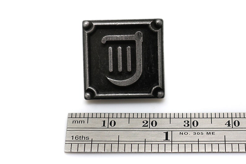 Puede incluir: Un pin de metal plateado con fondo negro y un s&iacute;mbolo de arpa plateado. El pin mide aproximadamente 2 cm de ancho.