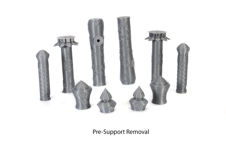 May include: A collection of nine gray 3D printed objects, some with intricate designs, before support removal.  The objects are arranged on a white surface.  Pre-Support Removal.