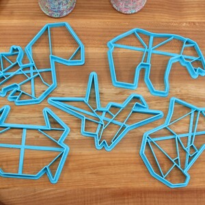 May include: Six blue plastic cookie cutters shaped like origami animals. The cutters are on a wooden surface.